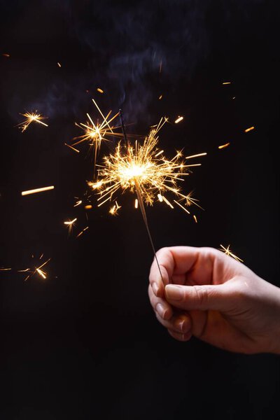 Вертикальный снимок руки с горящим бенгальским огнем на темном фоне