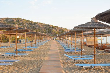 Güneşliklerle ve sazdan şemsiyelerle çevrili kumda dar bir patika..