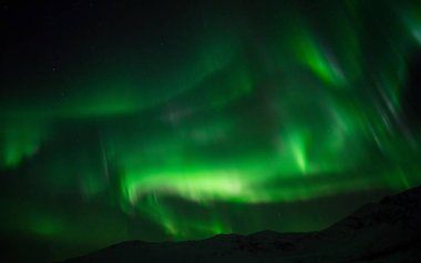Norveç 'te dağların üzerinden parlak yeşil bir Aurora manzarası.