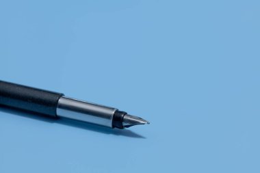 Mavi arka planda siyah plastik gövdeli ve metal aksanlı bir vektör kaleminin yakın çekimi.