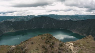 Quilotoa Volkanı 'nın tepesinde duran ve Göl Krateri' ne bakan birinin havadan çekilmiş bir fotoğrafı.