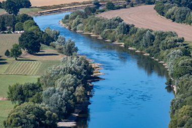 Kırsal alanda akan bir nehrin üst görüntüsü. Tarım arazileri ve yeşil bitki örtüsüyle çevrili.