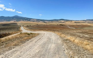 Mavi gökyüzünün altında, İtalya, Toskana 'da, arkasında dağ olan bir çöl arazisinde bir yol.