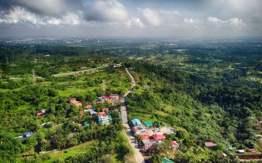 Renkli çatıları ve yeşil ağaçlarla çevrili bir yolu olan binaların üzerinden havadan çekilmiş bir görüntü.