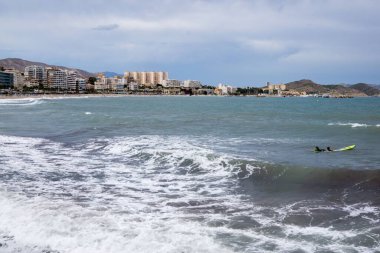 Deniz dalgaları kıyıya vururken şehir arka planda, Alicante, İspanya