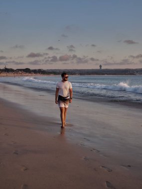 Arka planda mavi deniz olan beyaz gömlekli beyaz bir adamın sahilde poz verişi.