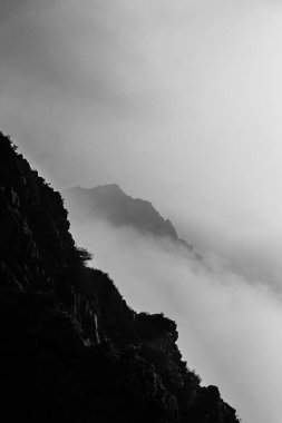 Keskin bir dağ yüksekliğinin dikey gri lekesi sisle kaplı kasvetli hava