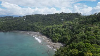 Deniz üzerinde bir hava görüntüsü ve bulutların altında yeşil yağmur ormanı sahili.