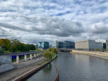 Berlin 'de bulutlu bir gökyüzünün altında nehir manzarası ve modern binalar.