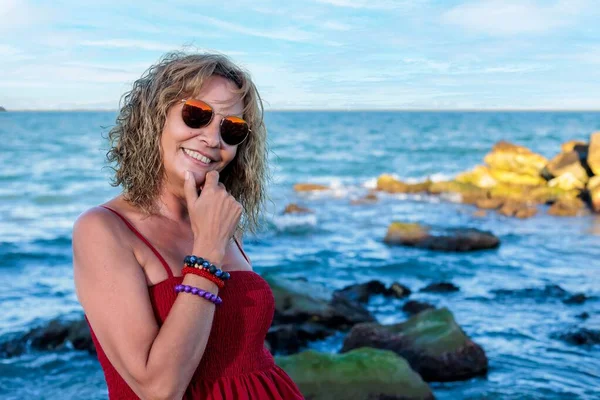 海に対して彼女の顎に手でポーズをとる彼女の50代の笑顔の女性のクローズアップショット — ストック写真