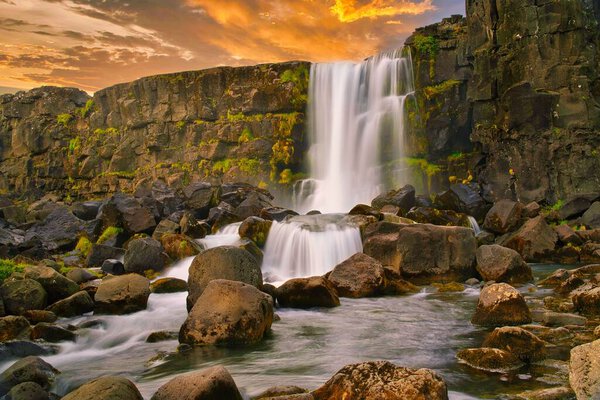 A beautiful view of a waterfall and stones in a river during sunset