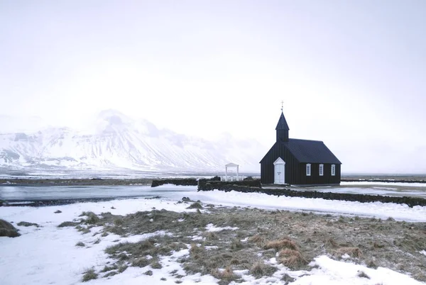 雪に覆われた高い山の前にアイスランドのBudakirkja教会の遠いショット — ストック写真