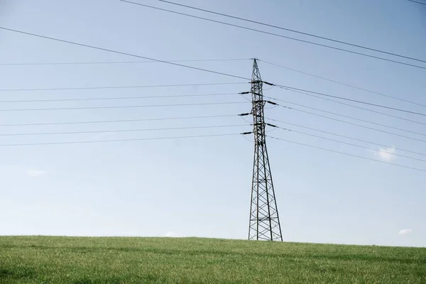 風景の中に送電塔 澄んだ青空の下の緑のフィールドにケーブルラインを持つ高電圧の電柱 — ストック写真