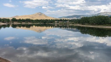 Bir dağın manzaralı görüntüsü, bitki örtüsü, ve bulutlu mavi gökyüzü Segovia, İspanya 'daki Pontoon Gölü' ne yansıyor.