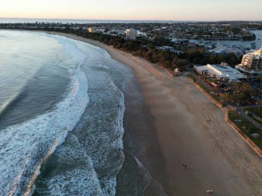 Kumlu bir sahilde köpüklü okyanus dalgalarının havadan görüntüsü.