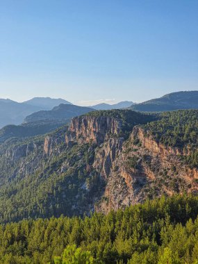 Fethiye ile Antalya arasında mavi gökyüzü altında ormanlık bir dağ sırasının manzaralı bir görüntüsü.