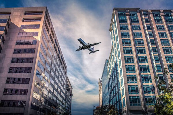A low angle shot of passenger plane flies over city buildings under blue cloudy sky