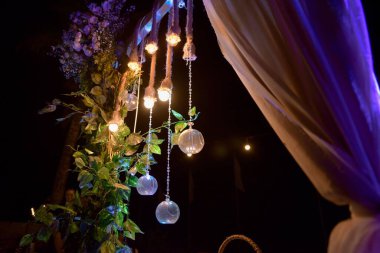 Yeşil yapraklar, çiçekler ve ışıklarla süslenmiş ahşap bir direğin alçak açılı görüntüsü.