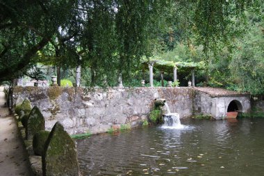 İspanya 'daki Pazo de Oca tarihi yapısında ağaçların altında küçük şelaleleri olan eski taşlı çitlerle çevrili bir nehir.