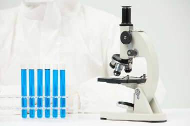 Tıp laboratuarında optik mikroskopla çalışan bir doktor ve masada test tüpleri var.
