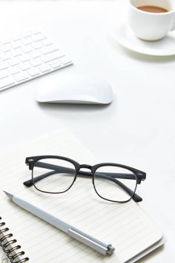 Not defteri, bardaklar ve bir fincan kahve olan beyaz bir ofis masasının dikey görüntüsü