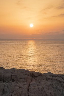 Batan güneşin dikey görüntüsü ve bir uçurumun önündeki turuncu renkli gökyüzü.