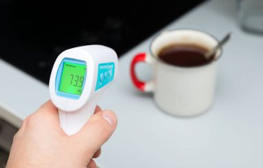 Temas edilmeyen tıbbi kızılötesi termometreye yakın çekim bir fincan kahveye karşı.