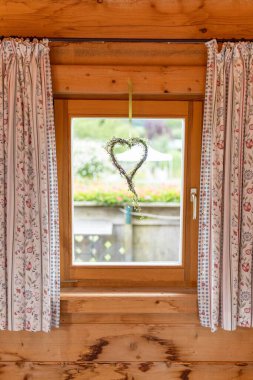 Ahşap pencereden sarkan dallarla yapılmış bir kalp şekli.