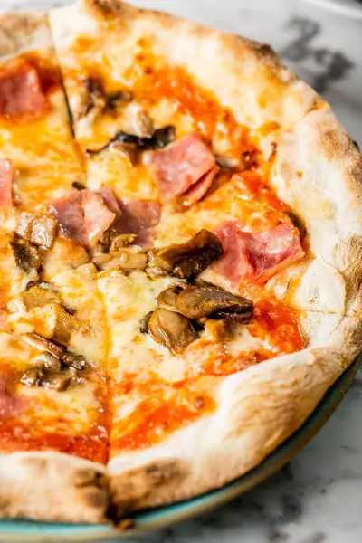 stock image A closeup of a pizza on the tablecloth, a napkin with knife and fork near