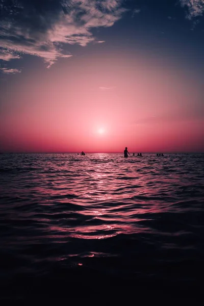 Вертикальный Вид Силуэты Людей Плавающих Море Величественным Красным Солнцем Светящимся — стоковое фото