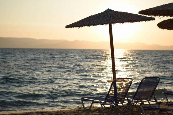 有选择的海滩椅子集中在草伞下 背景是蓝色海的日落景观 — 图库照片
