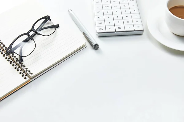A top view of a white office table with a notebook, glasses and a cup of coffee