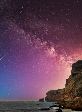 Sahildeki kayalıkların üzerinde güzel bir gece gökyüzünün dikey görüntüsü..