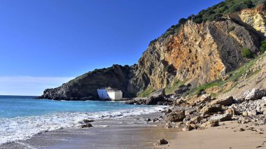 Praia da Mijona Sahili ve mavi denizin güzel manzarası Portekiz 'de açık gökyüzünün altında kayalık tepelerle çevrili.