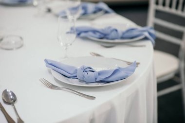 Bir düğün yerinde gümüş çatal bıçak ve tabaklarla kurulmuş bir masanın yakın plan fotoğrafı.