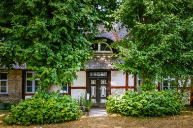 Yeşil ağaçlarla çevrili küçük bir köyde sazdan çatılı güzel bir papazın cephesi.