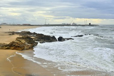 Arka planda sanayi kenti olan manzaralı kayalık bir deniz manzarası.