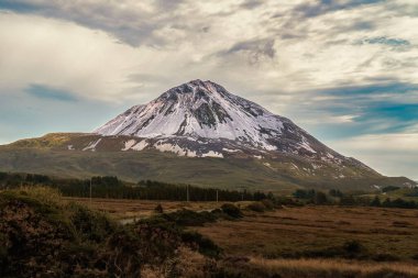 Donegal 'de bulutlu bir günde Errigal dağının yamaçlarından önce ağaçlarla kaplı kırsal alanlar