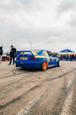 Sürüklenme yarışması sırasında sürüklenen bir pistte mavi ayarlı bir BMW spor arabanın dikey görüntüsü.