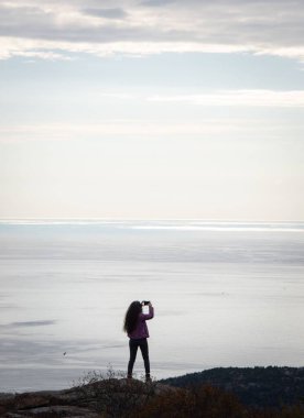 Sahilde durup denizin fotoğraflarını çeken bir kadının dikey görüntüsü..