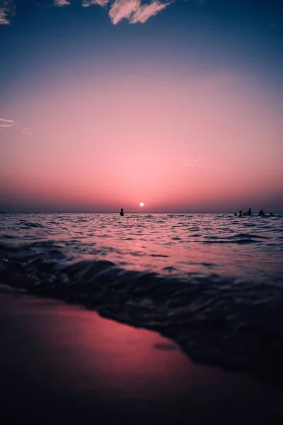 背景には雄大な赤い太陽が輝く海で泳ぐ人々のシルエットの垂直ビュー — ストック写真