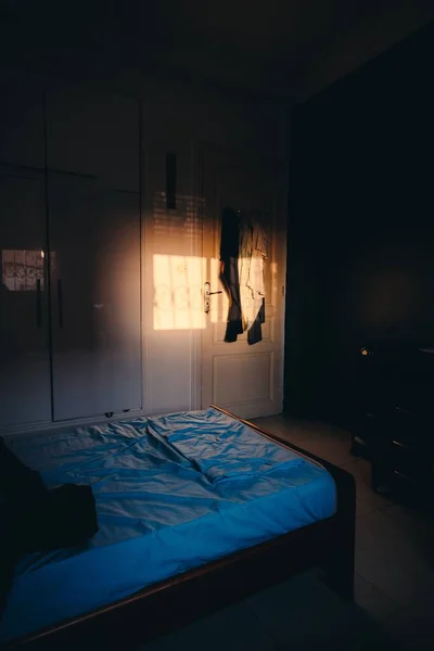 窓から服を着てドアに輝く太陽の光と空の暗い寝室の垂直 — ストック写真