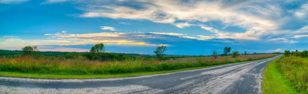 アスファルトの道路と緑の芝生のフィールド上の曇り空 — ストック写真