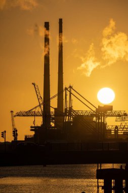 Gün batımında suyla çevrili bir sanayi bölgesinin dikey görüntüsü.