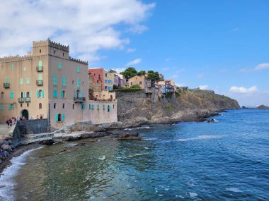 Mavi bulutlu gökyüzünün altında deniz kıyısındaki binalar ve kayalık uçurumlar