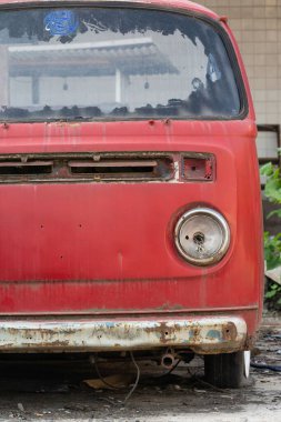 Bulanık arka planda eski, paslı, kırmızı bir arabanın ön kısmının dikey görüntüsü.