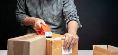 Adamın biri evindeki odasında online işlerinin küçük bir kutusunu paketliyor.