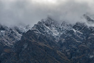 Queenstown, Yeni Zelanda 'da sisli bir günde karla kaplı kayalık dağ zirveleri