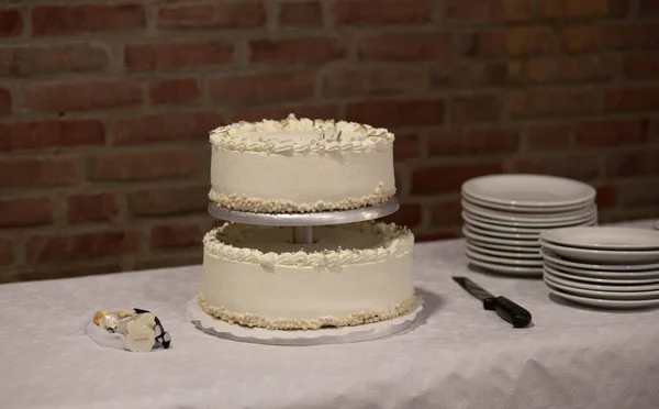 A white holiday cake next to the white plates, knife, and a cake topper on the table