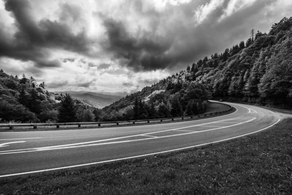 曇りの空の下で山のふもとに湾曲した道路のグレースケールショット — ストック写真